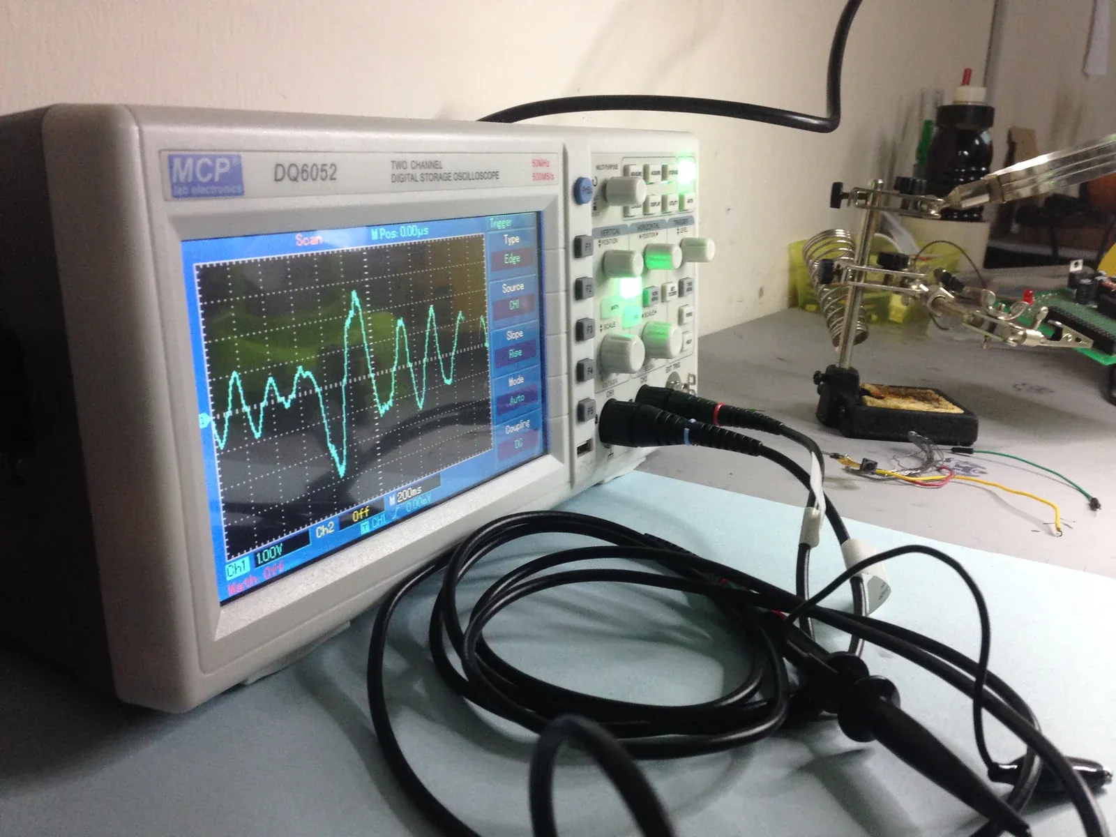 An oscilloscope reading a test signal on a REKA electronics bench